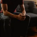 A young man sitting on a couch clasping his hands.