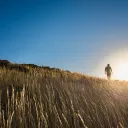 Um homem subindo uma colina gramada com o sol forte ao fundo.
