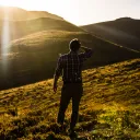 Um homem olhando para uma vista de colinas com o sol nos olhos.