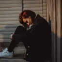 A young woman sitting on the ground hunched over as if she is struggling in life.