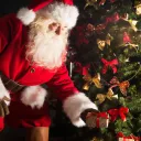 Santa Claus putting Christmas gifts by a tree.