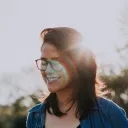 A young woman smiling with sun rays behind her head.