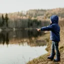 A little child standing by a lake pointing.