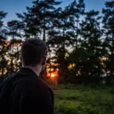 A man outside with the sun behind the trees.