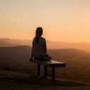 A woman sitting on a bench at sunset.