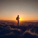 A man standing on a hill with the sun setting.