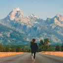 Photo of a person running towards mountains in the middle of an empty road.