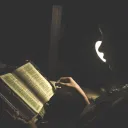 A person reading a Bible by a lamp.