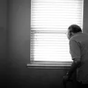 An elderly man looking out a window.