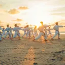 A group of people practicing martial arts moves on a beach.