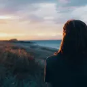 a woman standing with her back turned as she faces the sunset on the horizon