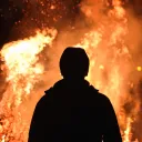 the silhouette of a person standing in front of leaping flames of fire