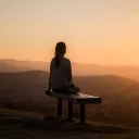 A woman sitting on a bench watching the sunset.