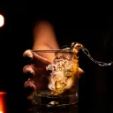 An extended hand holding a beer glass with liquid splashing over the side