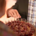 a man's hand reaching for a shot glass with red wine on a tray of similar glasses