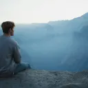A young man sitting on rock looking out over a valley.