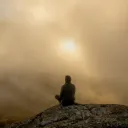 A person sitting on a rock in the morning fog.