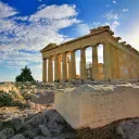 Ancient ruins of the Parthenon with tourists by the structure and a large block of stone in the foreground