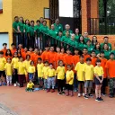a large group of people standing outside, some lined up on a staircase, some in front of it, all wearing one of three colors of matching shirts