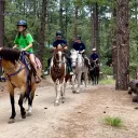 a group of girls riding horses in the woods