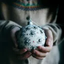 a woman holding a christmas ornament and wearing a seasonal sweater