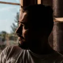 a concerned man looking out through a window, his face in shadow