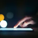 A finger touch the lit screen of an electronic device.