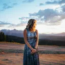 a woman wearing a long dress looking towards the sunset and she stands outside in a field