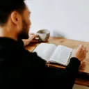 A man reading a Bible with his phone nearby.