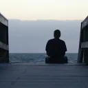 A person sitting at the end of a beach pier looking out at the water.