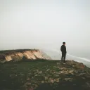A man looking over a cliff toward the ocean.