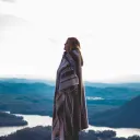A woman wrapped in a blanket standing outside with mountains in the background.