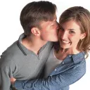 A young man kissing a young woman who is hugging him.