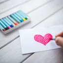 A person drawing a red heart with a crayon.
