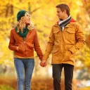 A man and woman holding hands walking in a park in the fall.