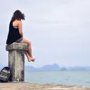woman sitting on post looking at water