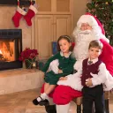 Two children sitting with Santa Claus in front of a Christmas tree.