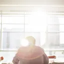 A person sitting at a table with sun rays coming in from a window.