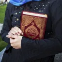 Woman holding a copy of the Quran in her arms.