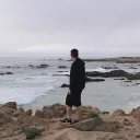 A man walking on a rocky shore of the ocean.