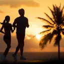 Man and woman running on beach with a palm tree in the background.