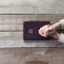 A person with their hands on top of a Bible that is on a table.