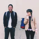 Two young adults waiting for a bus - both with smiles on the faces.