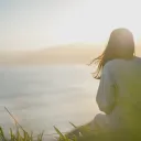A young woman looking over water with the sun in the background.