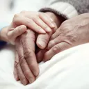 A young pair of hands comforting an elderly hand.