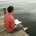 A man sitting on a dock reading a Bible.