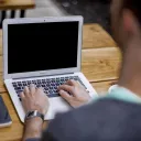 A man typing on a laptop while sitting a desk.
