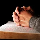 Hands clasped onto of a Bible as if person is praying.