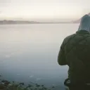 A young man standing by a lake.