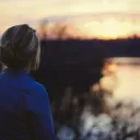 A young woman looking at the sun setting over water.